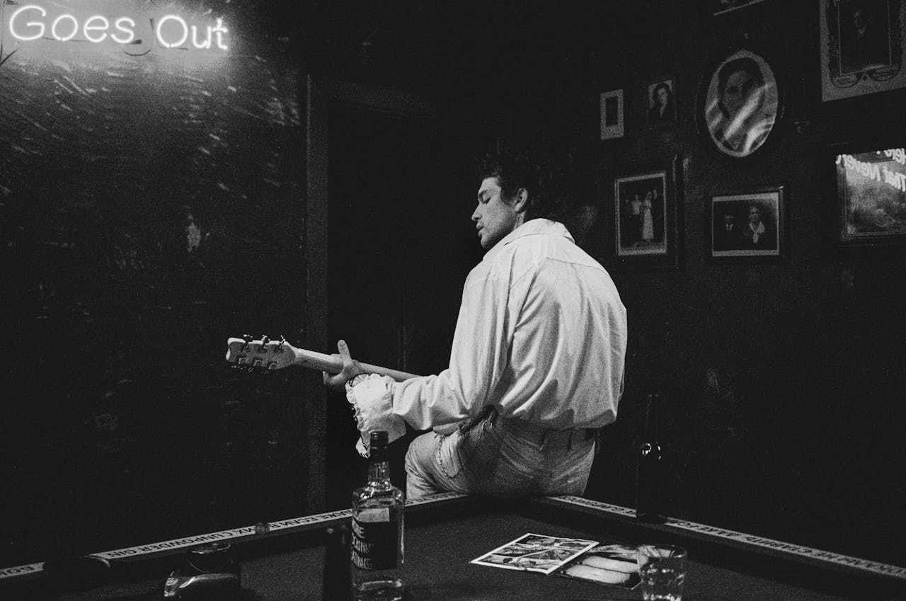 about-02 A musician at a bar playing guitar with a moody atmosphere in black and white.