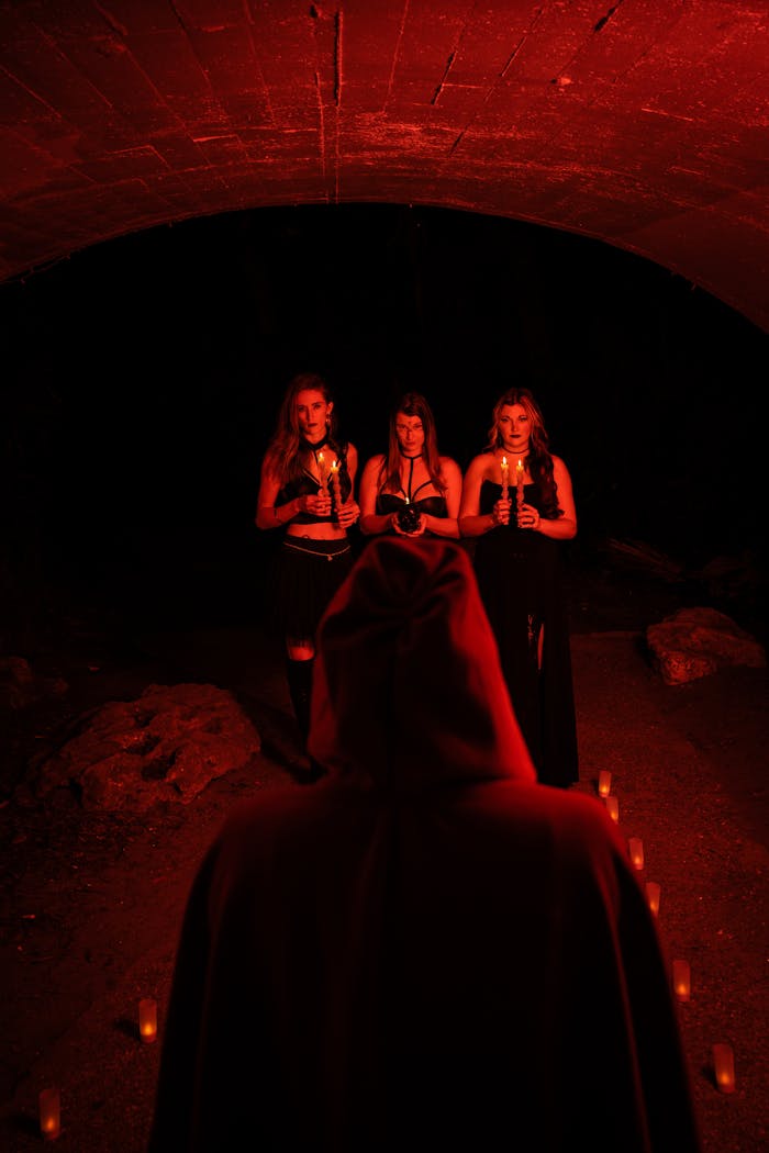 menu-03 Spooky scene of three women holding candles in a dark, red-lit underpass during Halloween.