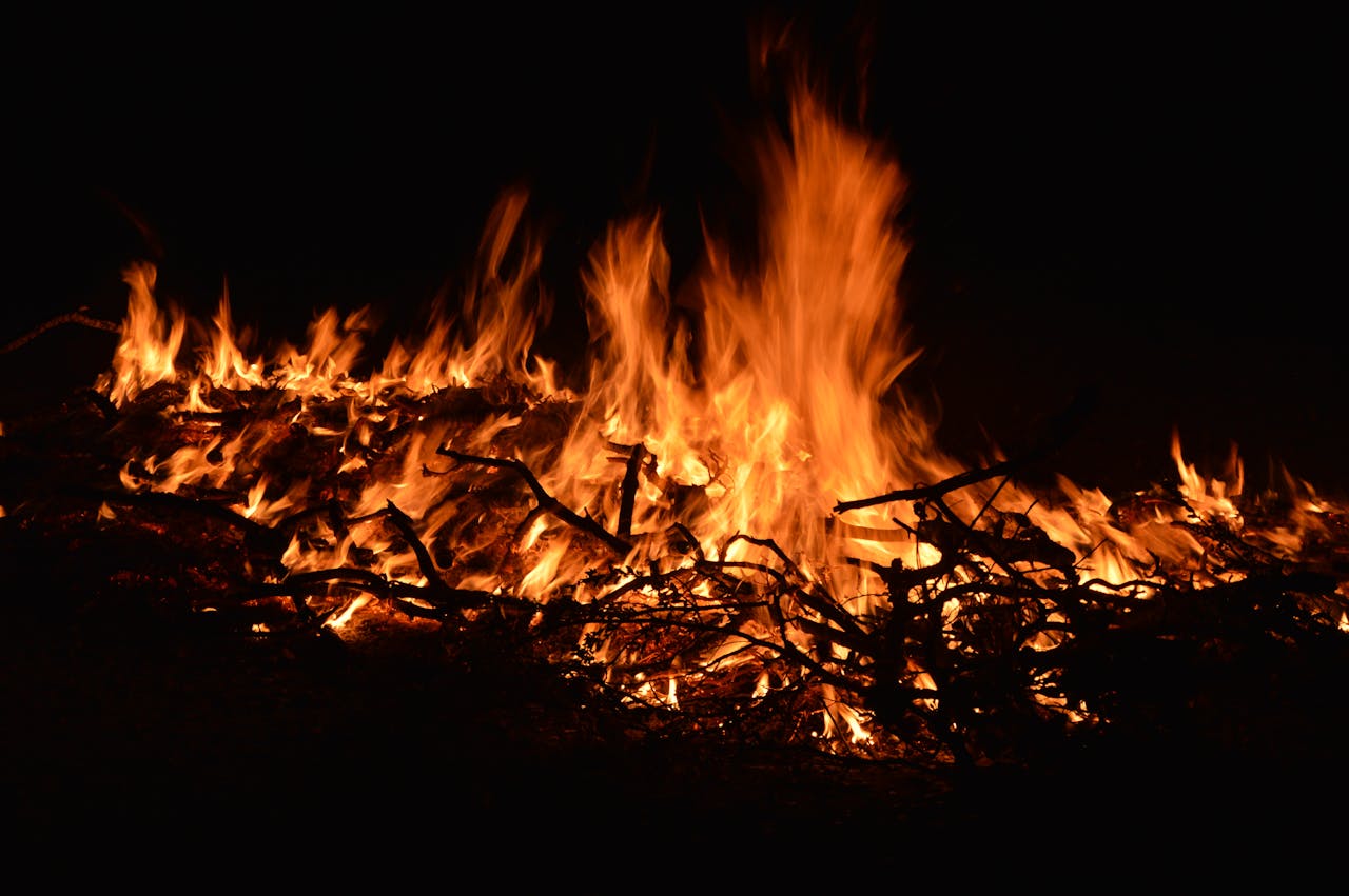 A close-up view of a large, blazing bonfire at night, with fiery flames and embers.