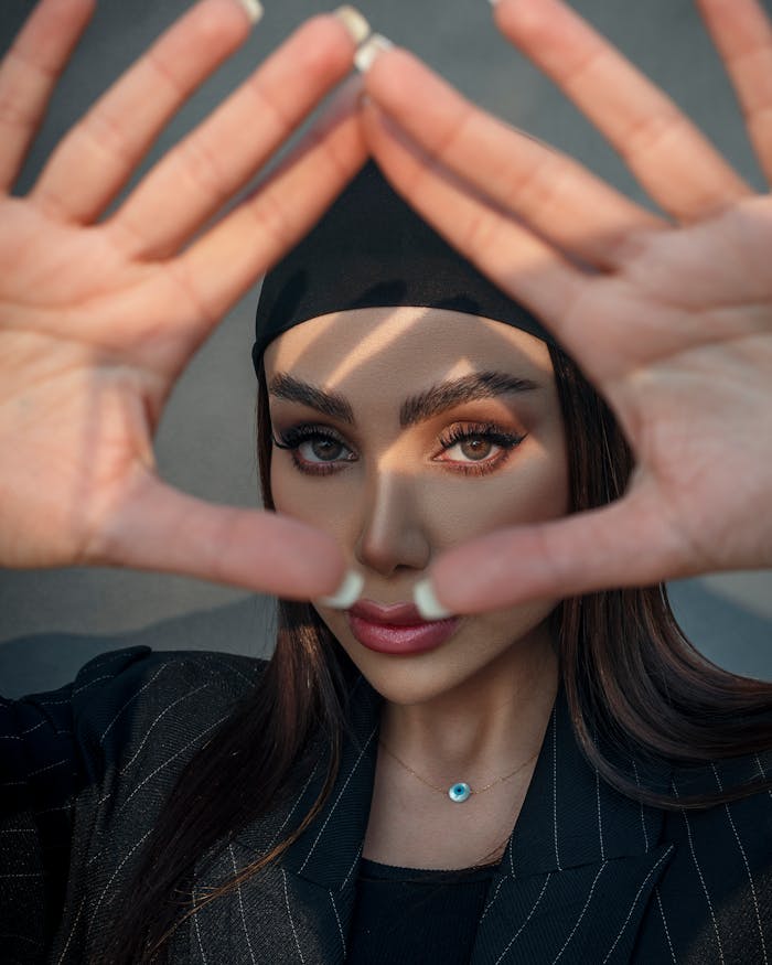 Fashionable young woman posing with hands forming a triangle shape, emphasizing modern style and beauty.